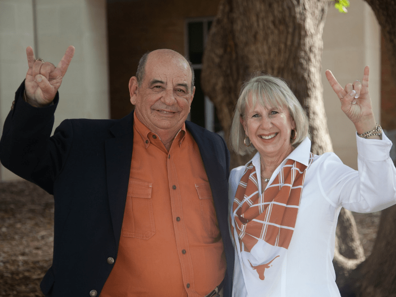 Tom and Mimi McKnight embracing and doing hook 'em horns hand sign