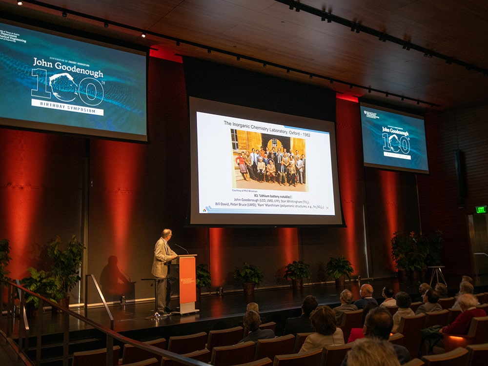 Speaker giving presentation at podium with slideshow projections