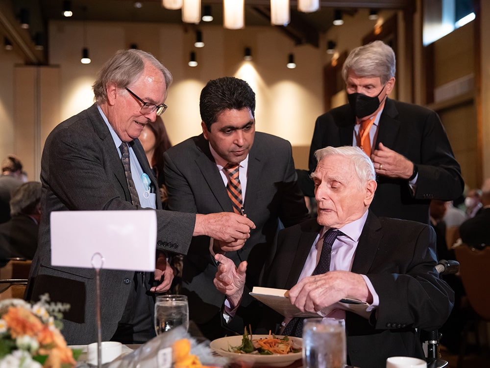 John Goodenough seated at dinner with three men talking to him