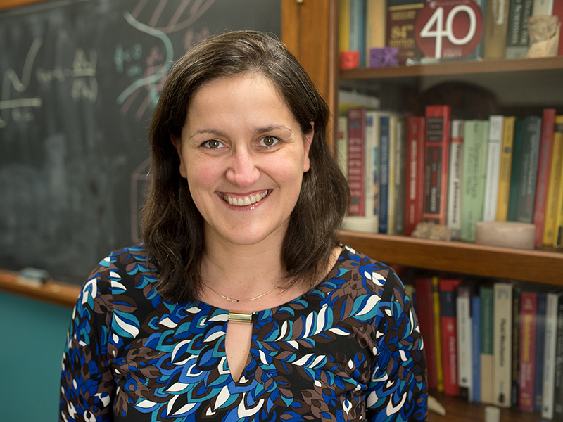 Masa Prodanovic smiling in front of a chalkboard and bookshelves