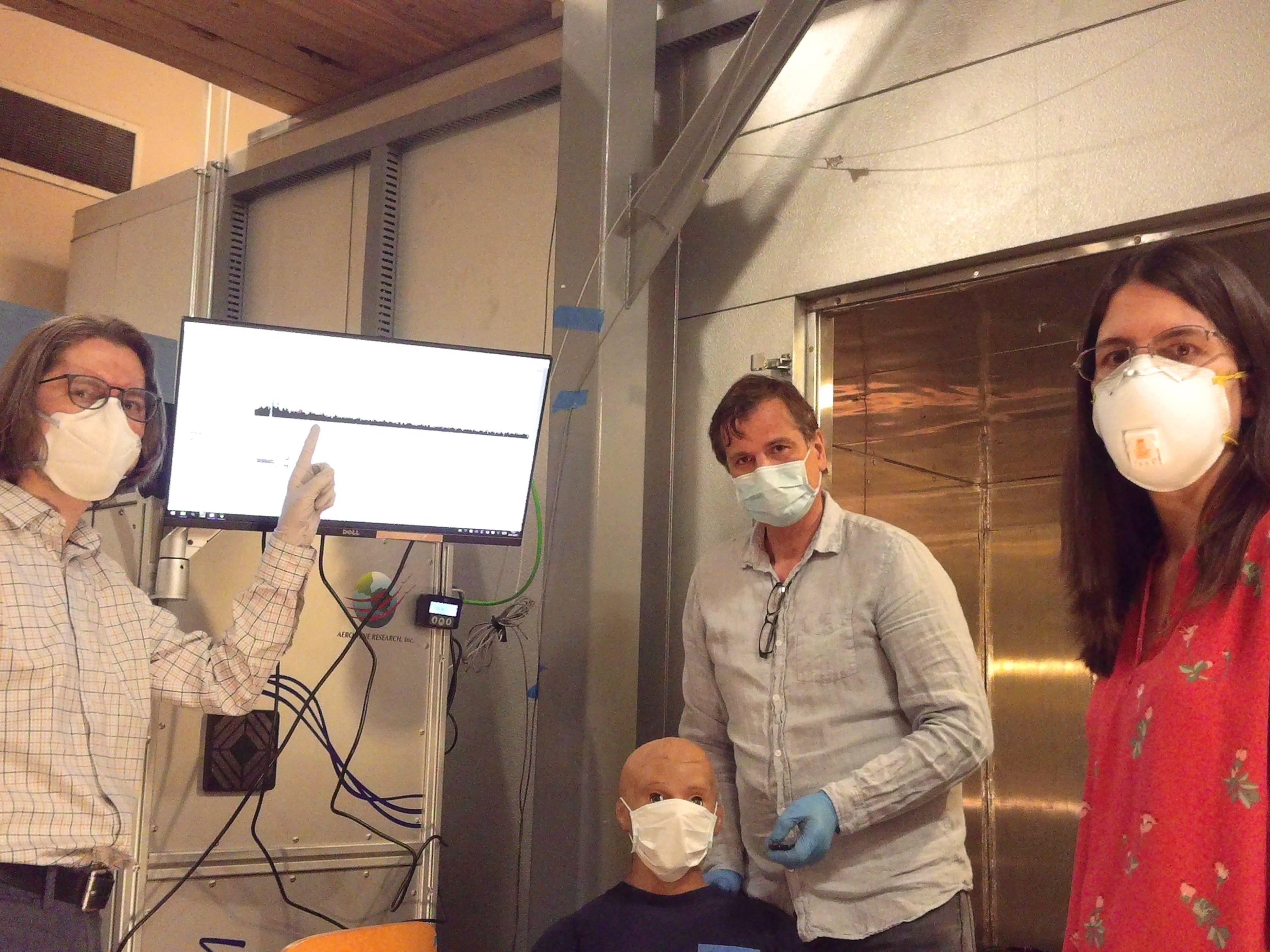 Three researchers pose in lab with dummy while all wearing masks 