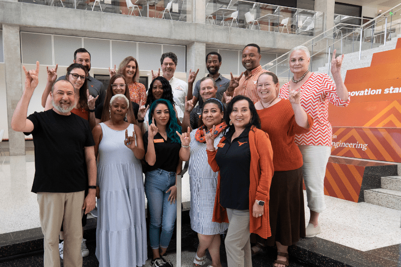 Cockrell School Staff Council smiling and doing hook 'em horns by staircase