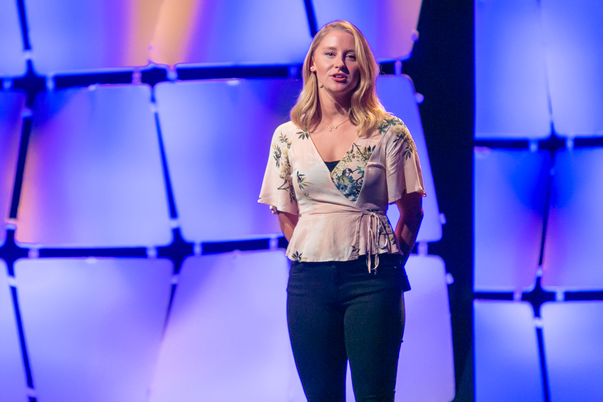 woman standing on stage talking into head microphone