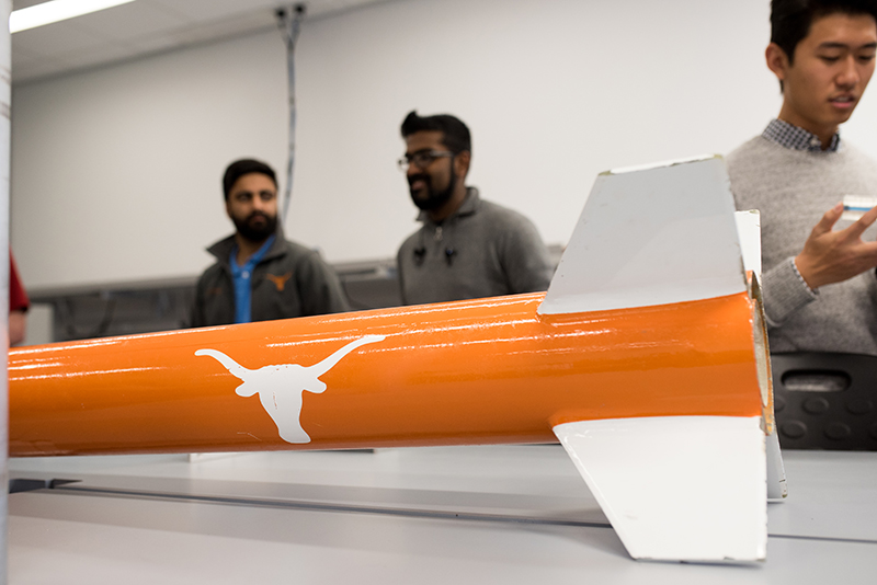 close up of new rocket with UT students in background