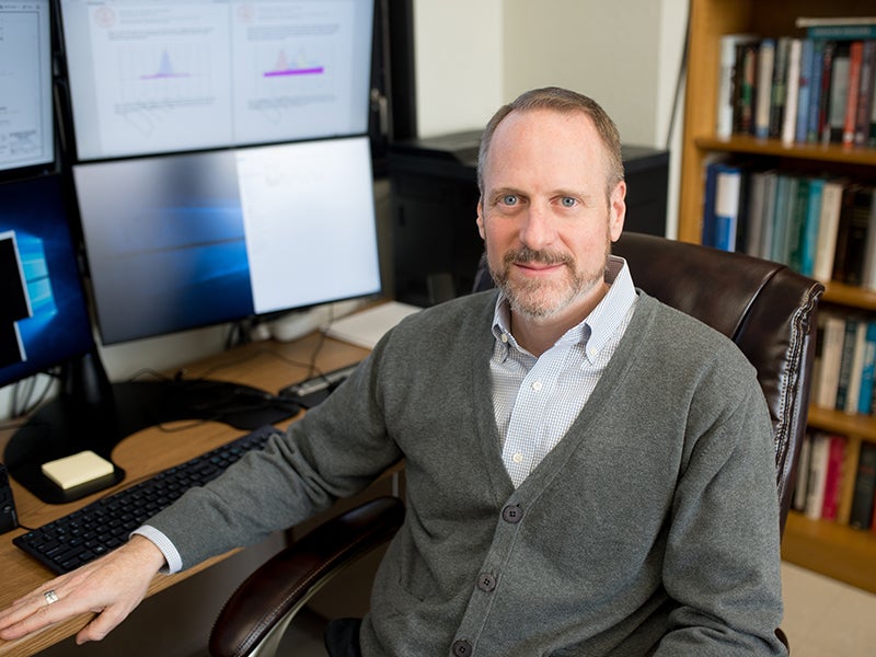 Texas Engineer William Charlton smiling in front of computer monitors and a bookshelf