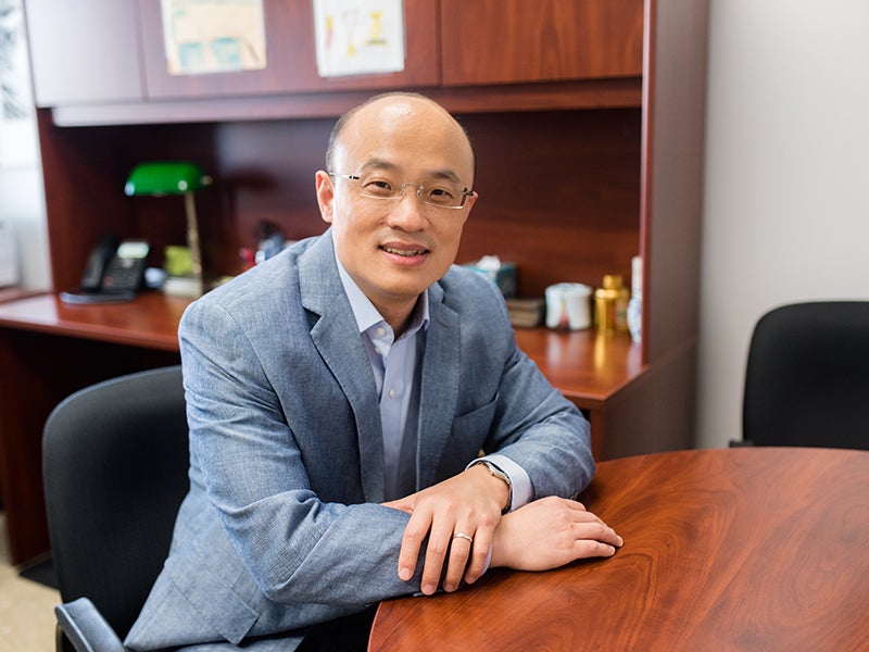 Texas Engineer Junmin Wang smiling seated at a large oak table