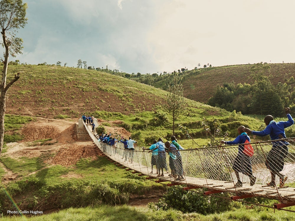 people crossing footbridge over green ravine