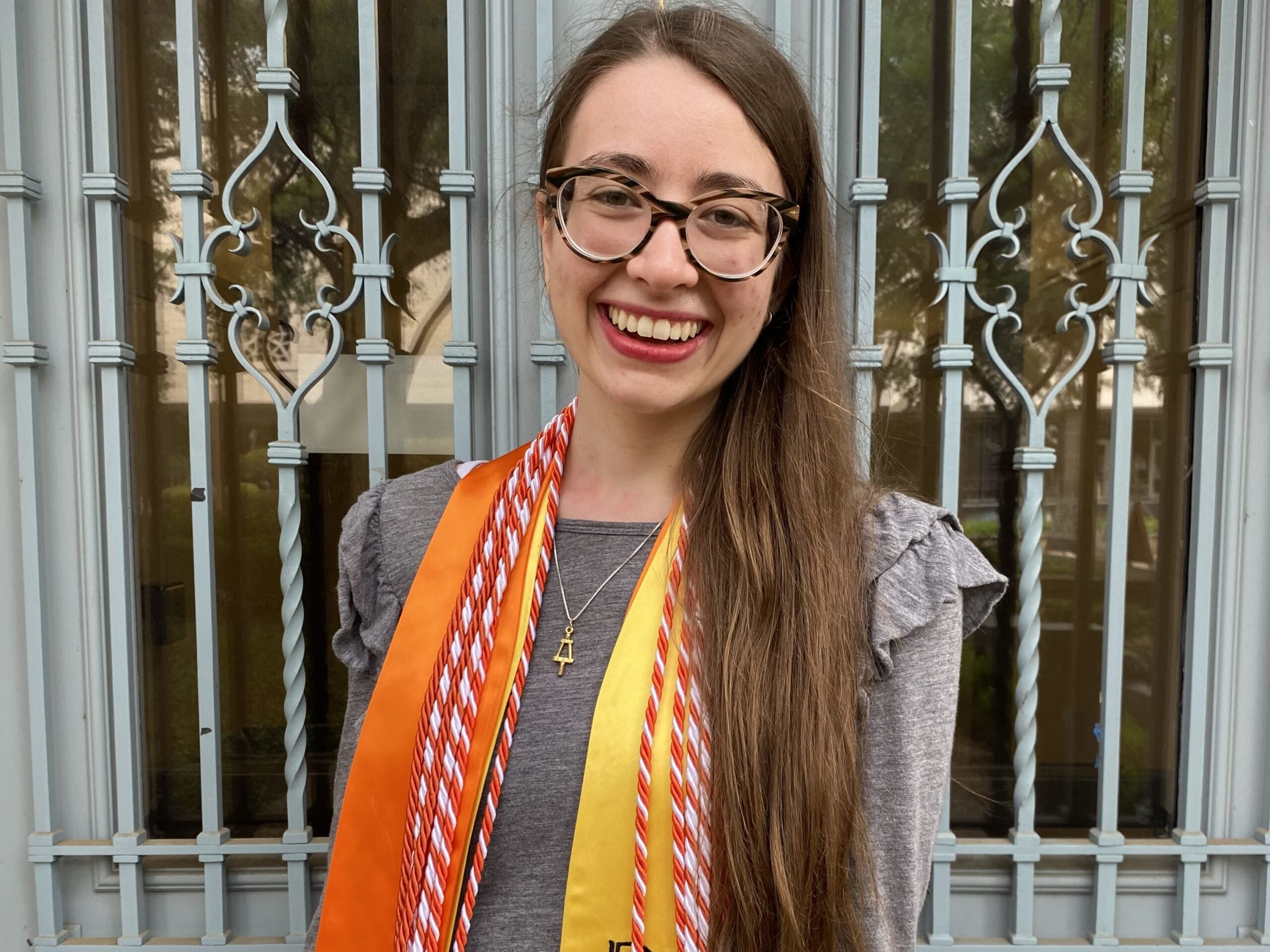 Texas Engineer Katharine Fisher standing in front of door while wearing graduation regalia.