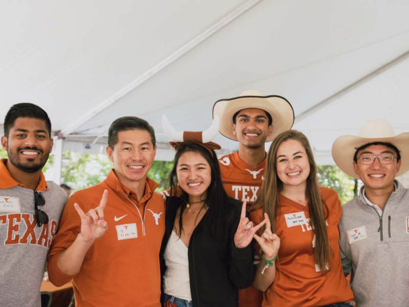 Texas Engineering alumni smiling and doing hook 'em hand signs at UT Austin tailgate
