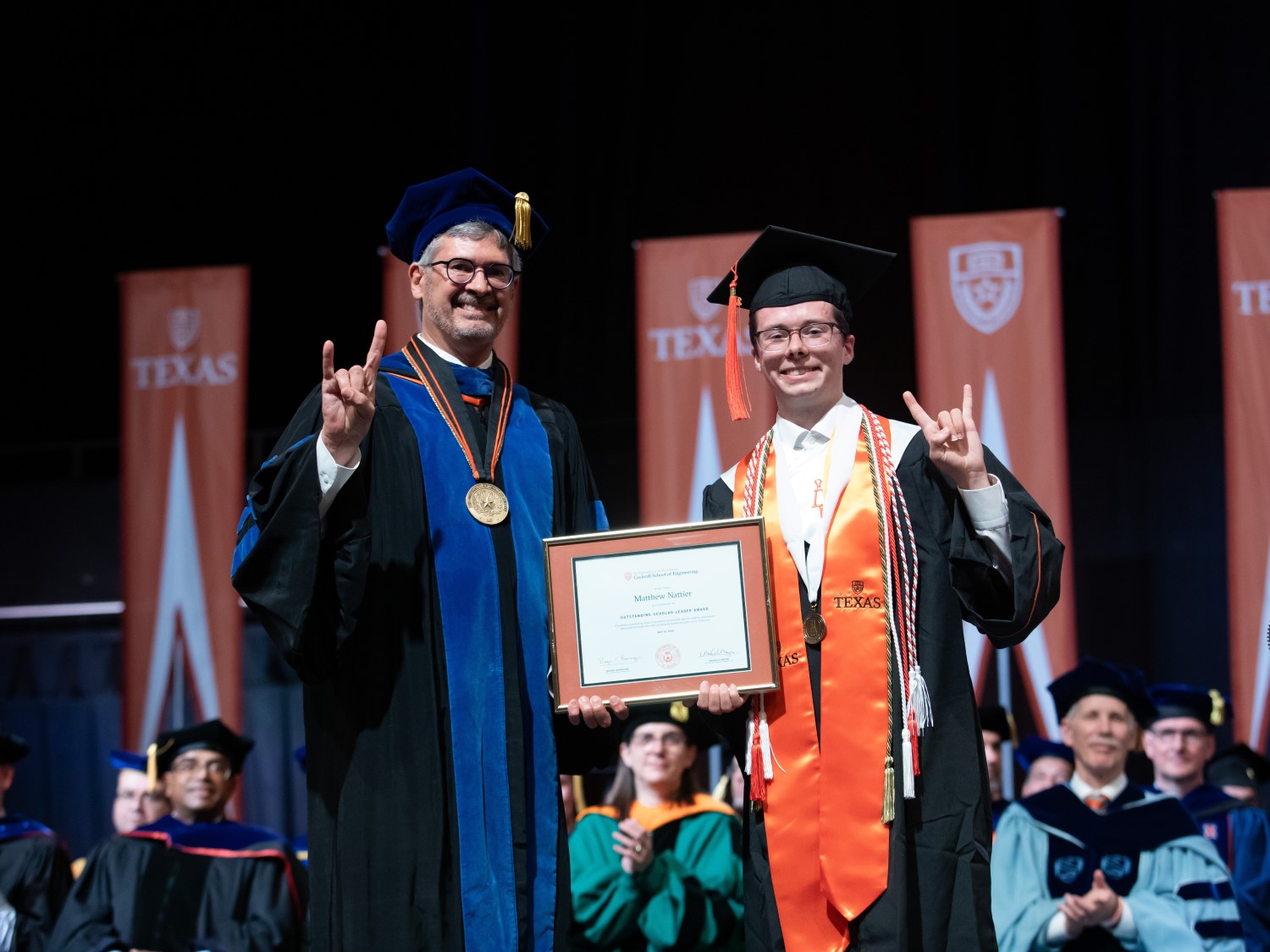 Texas Engineer Matthew Nattier on stage at Commencement with Dean Roger Bonnecaze doing hook 'em horns hand sign