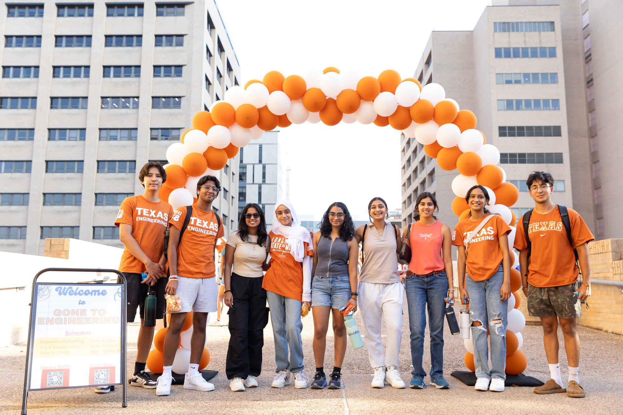 Undergraduate students smiling and standing under balloon archway on the Forty Acres. 
