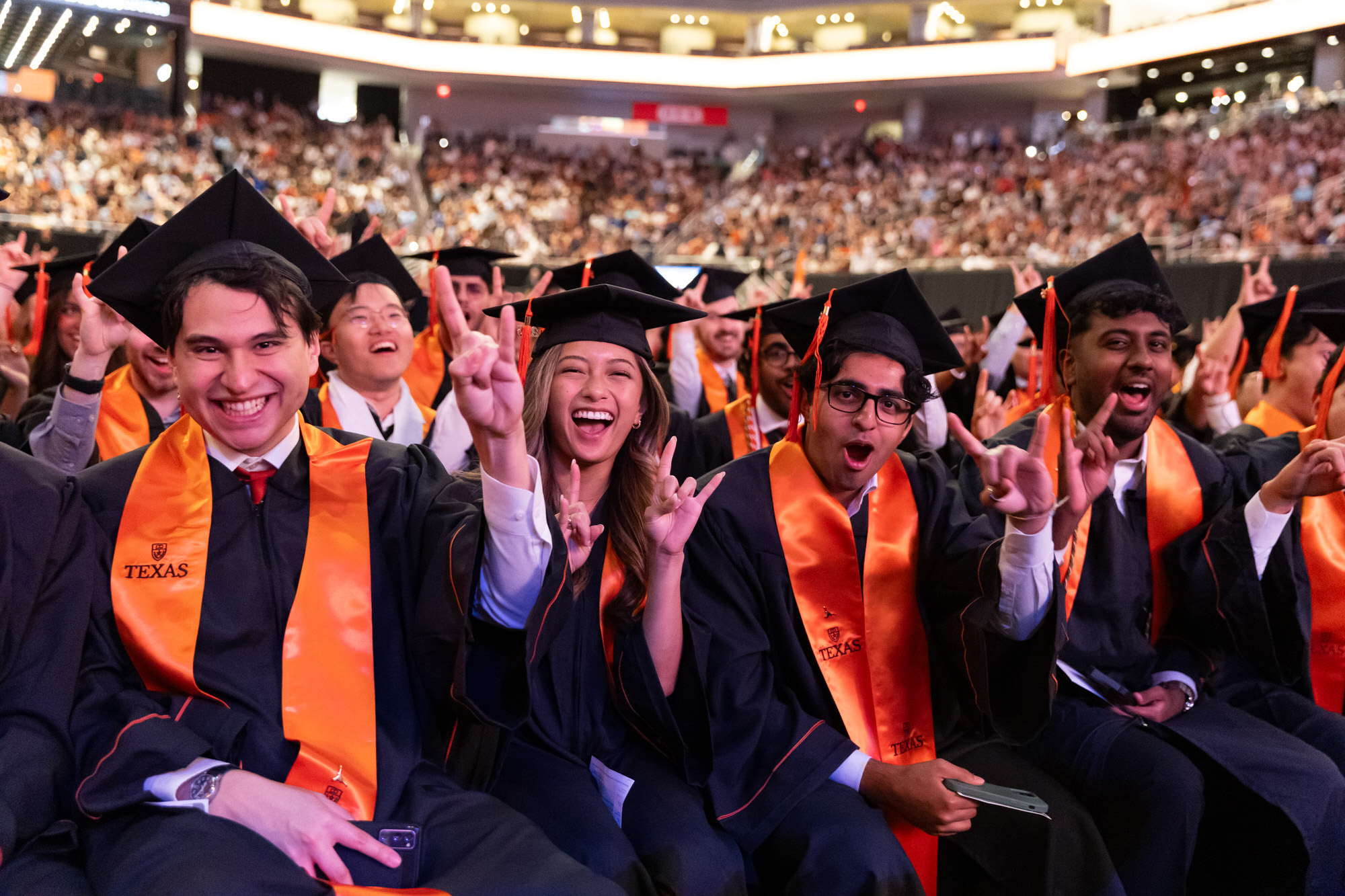 Undergraduates smiling and cheering at Commencement in caps and gowns.