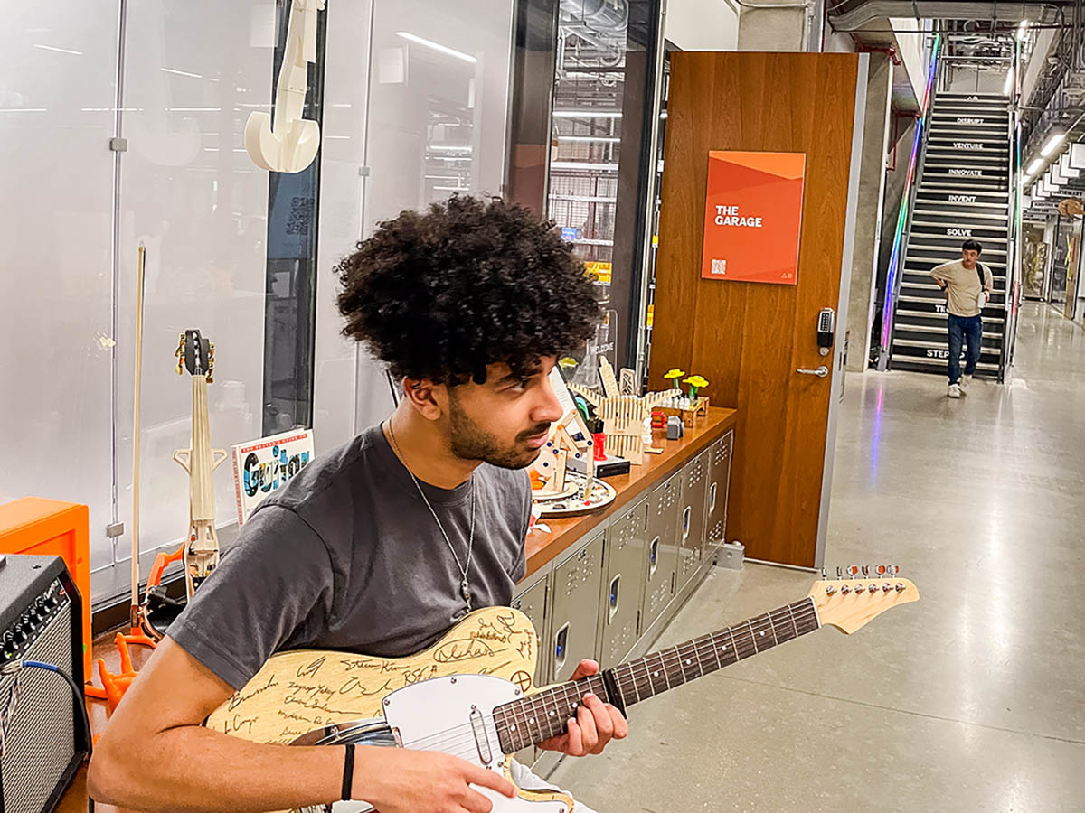 David DiBenedetto sitting on a stool playing a guitar he crafted using machines housed in Inventionworks at UT Austin