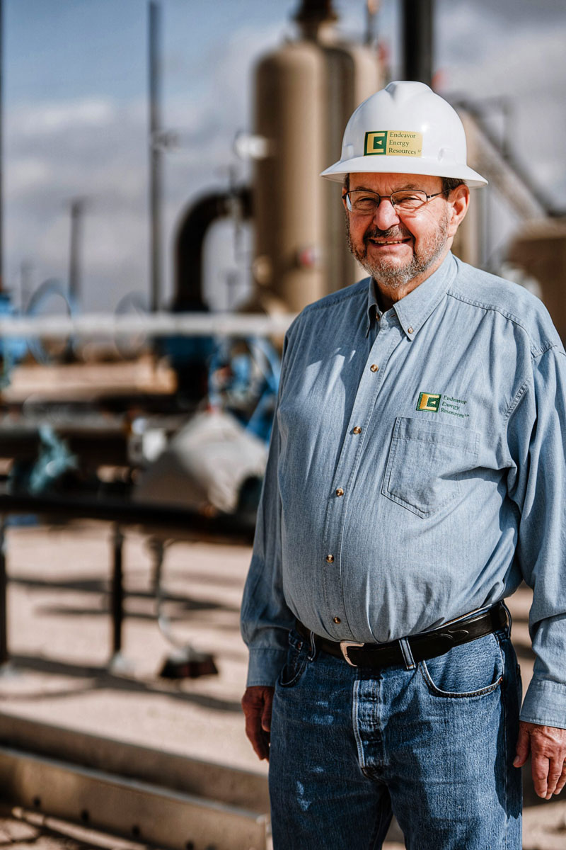 Autry C. Stephens stands in front of an oil rig wearing a white hard hat.