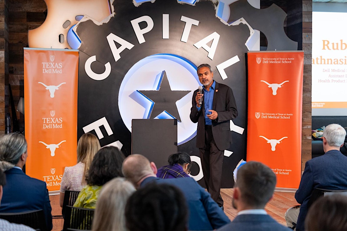 Dell Med researcher speaking in front of Captial Factory logo on stage flanked by Dell Med banners