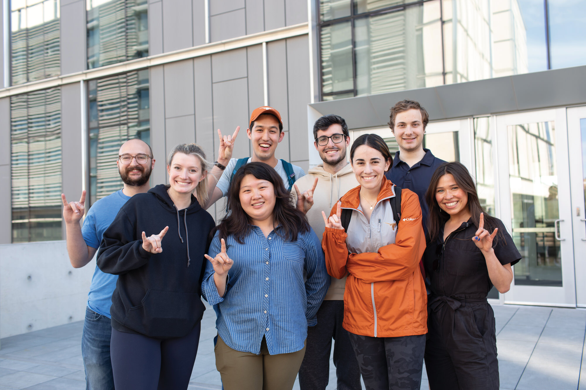 Texas Engineers smiling outside GLT building doing hook 'em horns hand signs
