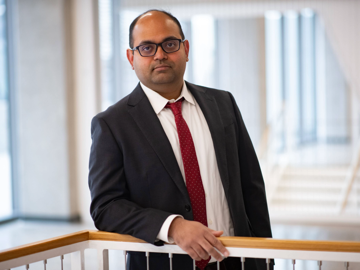Arvind Ravikumar holding stair railing in brightly lit hallway.
