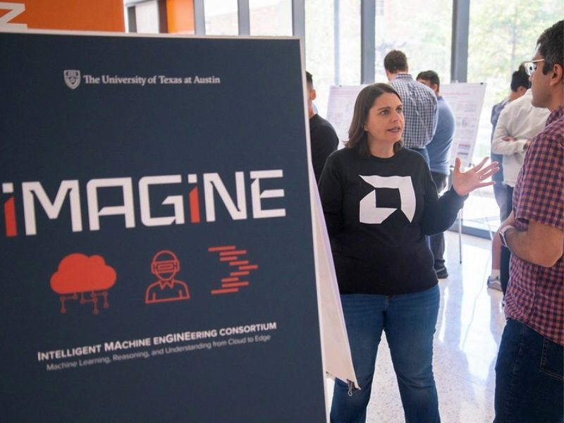 Woman talking to event attendee in front of iMAGiNE poster