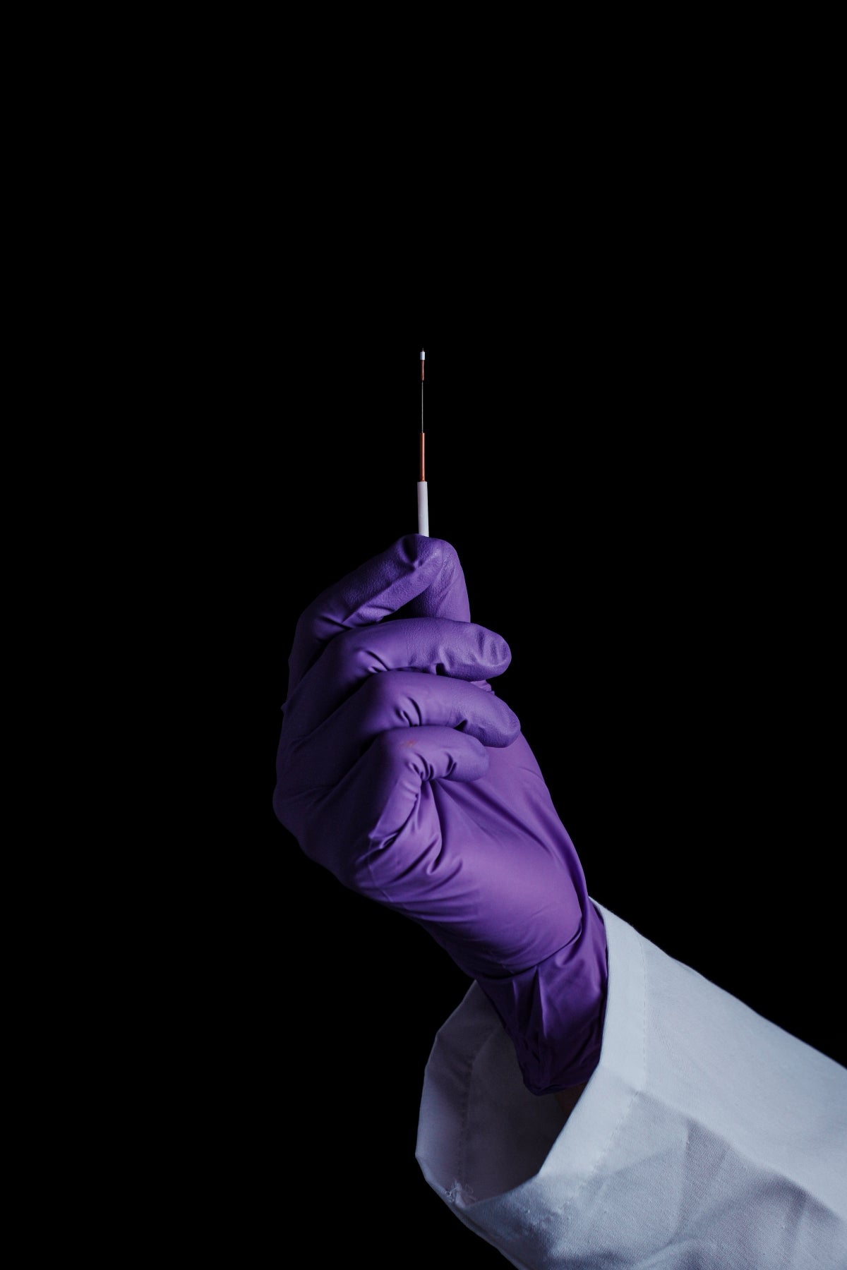 A gloved hand holds a tiny biomarker probe.
