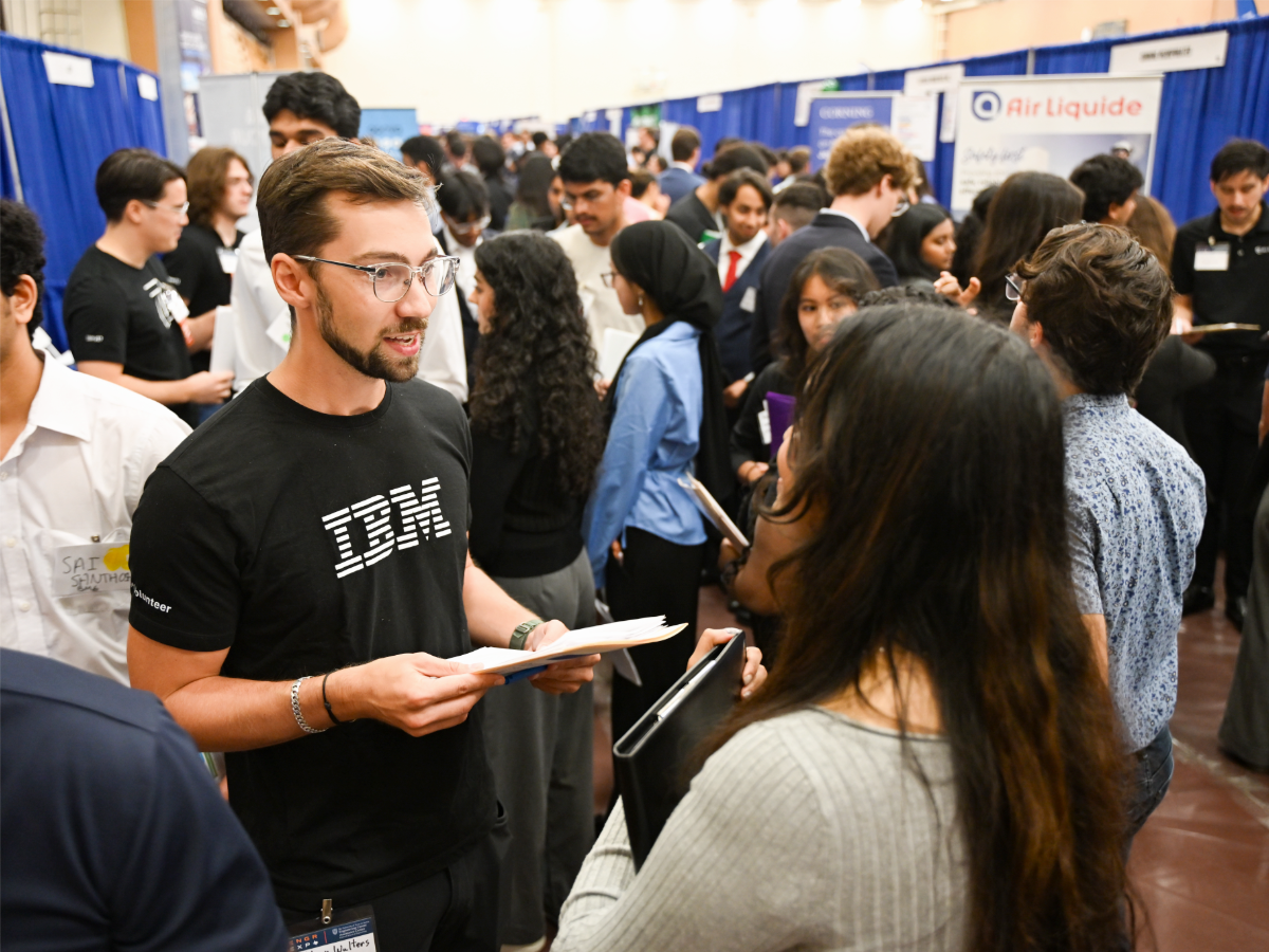 Industry representative talking to Texas Engineering student during crowded Engineering Expo event