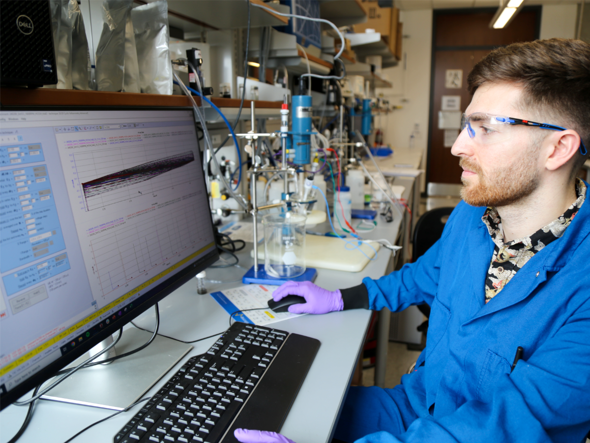 Texas Engineering researcher wearing lab safety gear typing at computer monitor