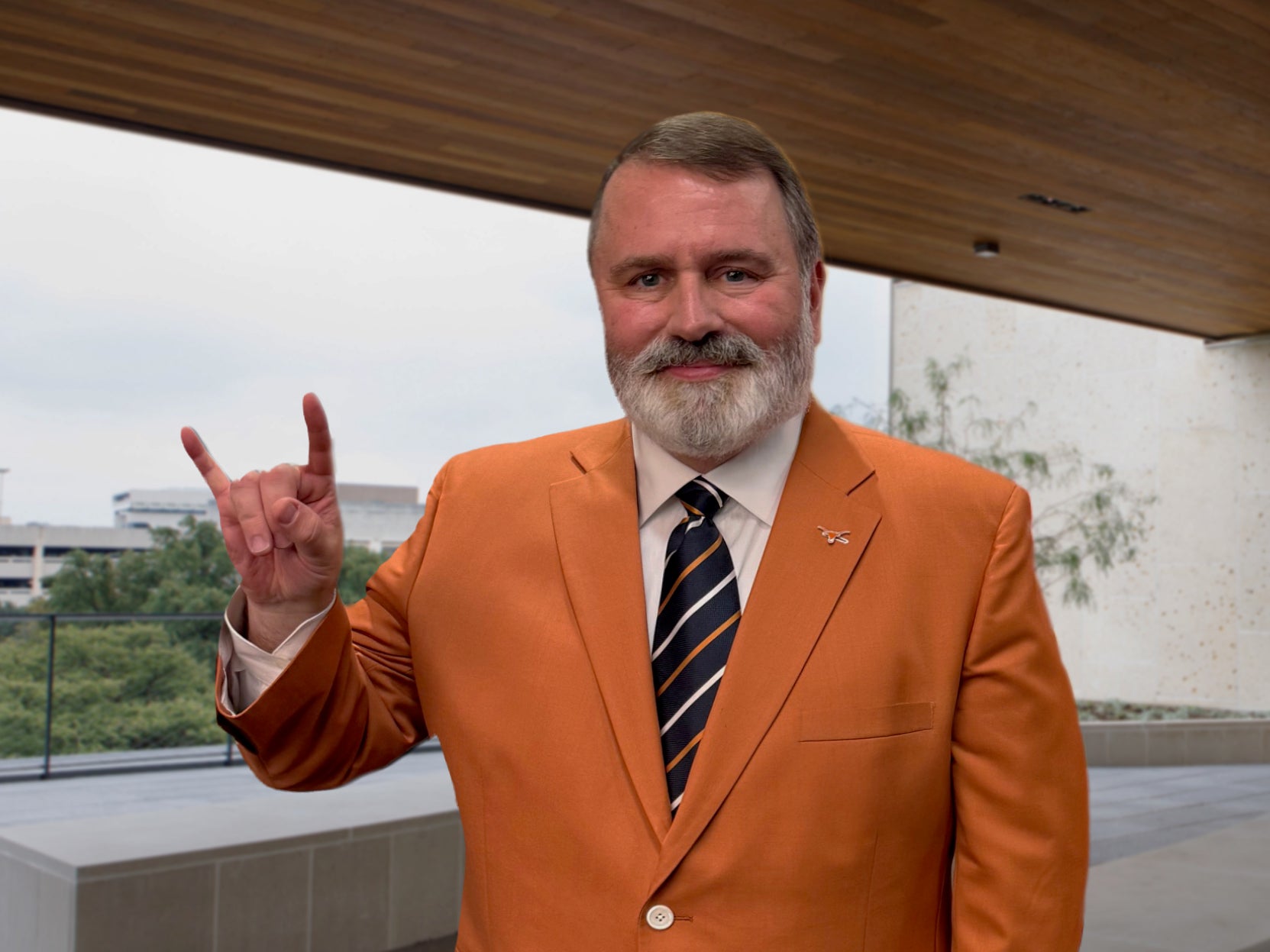 Dan Deans in an orange jacket showing a hook 'em hand sign