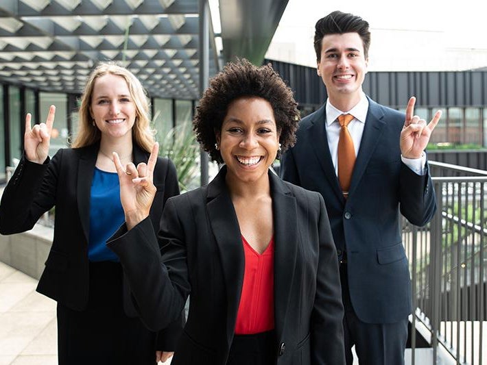 Students dressed in business suits doing hook 'em horns hand sign