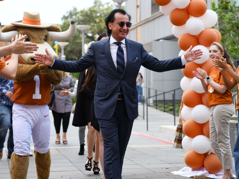Fariborz Masseh walks though a balloon arch with Hook Em, UT Austin's mascot.