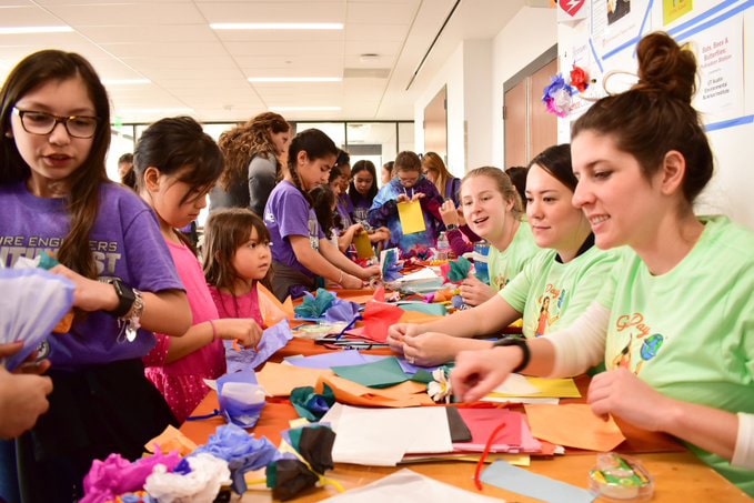 Texas Engineers and K-8 female students working on projects at a table at UT Austin's STEM Girl Day