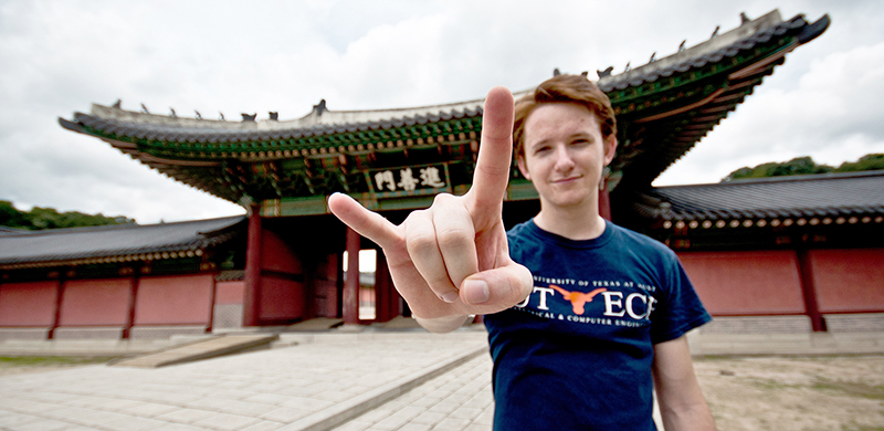 Texas Engineer smiling in front of building in Japan doing hook 'em horns hand sign