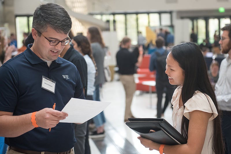 Texas Engineering student talking to recruiter in main EER building while he looks at her resume.