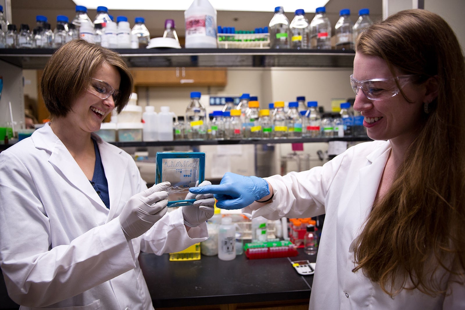 Texas Engineers laughing in lab while pointing to handheld research prototype